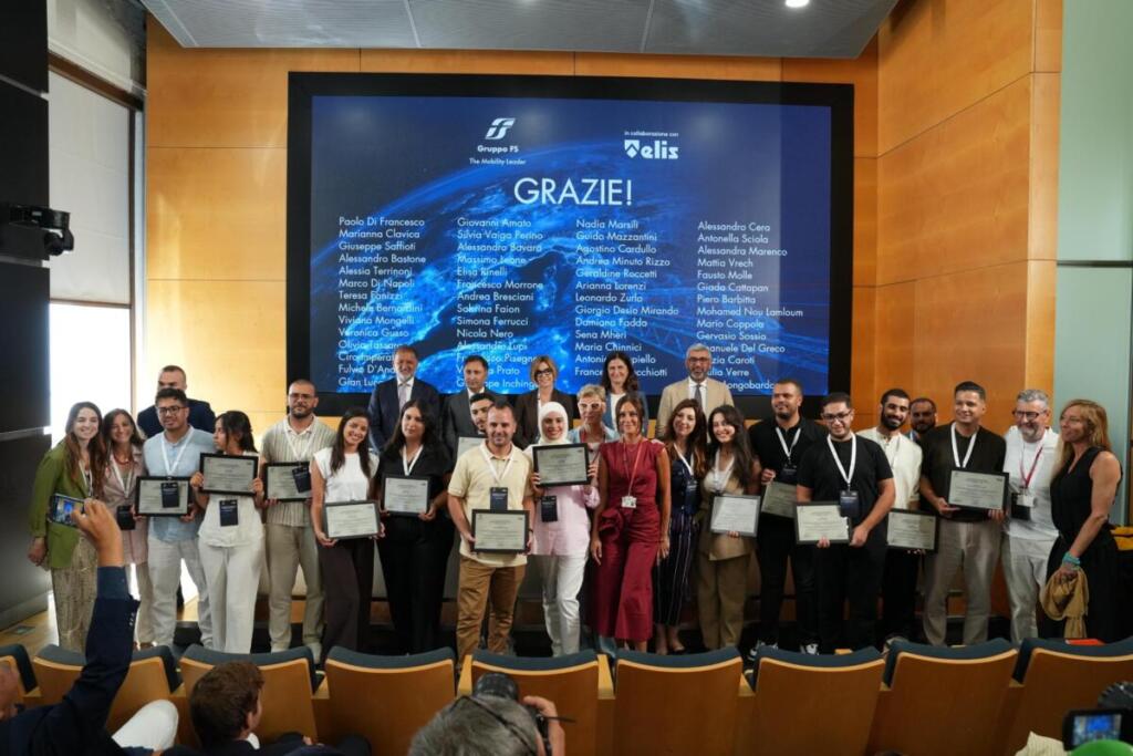 Quattordici cittadini tunisini hanno iniziato la propria esperienza professionale in Trenitalia dopo un percorso formativo svolto nel Paese nordafricano. Il progetto costituisce uno dei primi risultati delle iniziative che il Gruppo FS ha sviluppato nell’ambito del Piano Mattei e che ha presentato a Roma, nella sede di Villa Patrizi, durante la cerimonia ‘Benvenuti in Italia – Piano Mattei Tunisia’. Il programma ha unito preparazione linguistica, educazione civica, sicurezza sul lavoro e addestramento tecnico. I partecipanti hanno seguito oltre 400 ore di italiano per raggiungere il livello B2, 150 ore dedicate al ruolo professionale e 24 ore riservate alla sicurezza. Dopo le verifiche sanitarie e amministrative, il gruppo ha raggiunto l’Italia e ha avviato l’inserimento nelle attività di supporto ai servizi ferroviari di Trenitalia. Le assegnazioni riguardano gli impianti di Trieste, Savona, Pisa, Cagliari, Napoli e Taranto. Prima della partenza il progetto ha previsto anche servizi di accompagnamento, potenziamento linguistico e sostegno all’integrazione sul territorio. Il modello tunisino punta su canali regolari di mobilità internazionale e collega la selezione dei candidati a un percorso che prepara sia al mestiere sia alla vita in Italia. La presenza dei tutor aziendali offre inoltre un riferimento durante le prime fasi dell’attività. Lo scopo è un inserimento lavorativo stabile. La cerimonia ha riunito rappresentanti delle istituzioni, del Gruppo FS, di Trenitalia e dell’Ambasciata tunisina. Sono intervenuti Anna Veronica Gianasso, consigliera della Struttura di missione per l’attuazione del Piano Mattei; Giuseppe Inchingolo, Chief Corporate Affairs, Communication & Sustainability Officer del Gruppo FS; Gian Luca Orefice, Chief People, Culture & Transformation Officer; Francesca Stacchiotti, direttrice Risorse umane e Organizzazione di Trenitalia; Mohamed Amine Sayeb, consigliere politico dell’Ambasciata della Repubblica di Tunisia a Roma. “Sfida strategica” “Il Piano Mattei rappresenta una sfida strategica per costruire una cooperazione fondata su competenze, crescita condivisa e sviluppo sostenibile” le parole di Giuseppe Inchingolo. Il manager ha ricordato che il Gruppo FS mette a disposizione patrimonio industriale, tecnologia e professionalità, con l’obiettivo di rafforzare il dialogo tra Italia e Africa. “I progetti realizzati in Tunisia ed Egitto dimostrano come un grande gruppo industriale possa contribuire concretamente agli obiettivi del Sistema Paese”, ha aggiunto. Gian Luca Orefice ha richiamato il ruolo della qualificazione professionale: “La formazione è il punto di partenza imprescindibile per costruire percorsi di inserimento lavorativo efficaci e duraturi”. Secondo il responsabile People, Culture & Transformation, il progetto combina competenze, inclusione e crescita professionale e crea le condizioni per un’integrazione basata sul lavoro e sulla condivisione delle conoscenze: “Un approccio che riflette pienamente i valori e la cultura del Gruppo FS, fondati sulla centralità delle persone, sullo sviluppo delle competenze e sulla capacità di trasformare il talento in opportunità di crescita condivisa”. Francesca Stacchiotti ha posto l’attenzione sul passaggio dalla formazione all’attività in azienda: “Il percorso avviato dal nostro Gruppo nell’ambito del Piano Mattei dimostra come gli investimenti nella formazione possano tradursi in opportunità concrete di lavoro e di crescita professionale”, ha spiegato. “Con l’ingresso in Trenitalia si apre una nuova fase, nella quale le competenze acquisite incontrano l’esperienza operativa e diventano parte integrante della nostra organizzazione”. Le strutture aziendali seguiranno il percorso e sosterranno l’integrazione dei nuovi lavoratori. Acquisizioni di competenze Il contributo del Gruppo FS al Piano Mattei comprende anche una linea di intervento in Egitto. Gli esperti di FS Engineering hanno curato un programma tecnico per docenti e studenti di istituti professionali locali. Le attività hanno riguardato la modernizzazione dei sistemi di segnalamento e controllo, la manutenzione dell’infrastruttura ferroviaria, la transizione energetica e l’adozione di nuove tecnologie. Il programma ha coinvolto gli istituti salesiani Don Bosco del Cairo e di Alessandria, con moduli rivolti agli insegnanti e a circa 60 studenti. Il confronto con gli specialisti di FS Engineering ha favorito l’acquisizione di competenze spendibili nel mercato del lavoro locale e ha consolidato la collaborazione tra i due Paesi nel settore ferroviario e infrastrutturale. Le iniziative in Tunisia ed Egitto seguono due direttrici complementari. La prima collega formazione e occupazione nel sistema ferroviario italiano; la seconda trasferisce conoscenze tecniche ai territori di origine. Entrambe si inseriscono nella cooperazione promossa dal Sistema Paese e vedono la collaborazione di ELIS, ente non profit attivo nell’orientamento, nella formazione e nell’innovazione tecnologica.